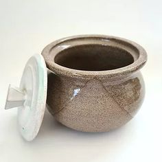 a small ceramic pot with a lid on the side, sitting on a white surface