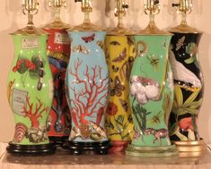 five vases are lined up on a mantle with gold candlesticks above them