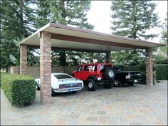 two pickup trucks parked under a covered parking lot next to a white car in the driveway