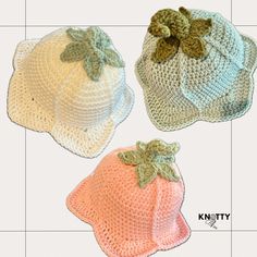 three crocheted hats with leaves on the top and one has a bow at the bottom