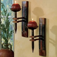 two candle holders are on the wall next to a vase with a plant in it