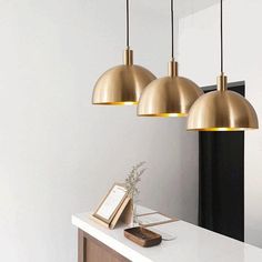 three brass pendant lights hanging over a white counter top next to a phone and notepad