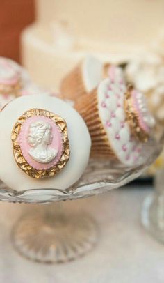 three decorated cupcakes sitting on top of a glass cake plate next to a wedding cake