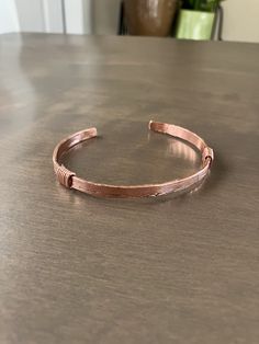 This solid copper bracelet was hammered from copper wire and accented with a gentle, lined pattern and is slightly distressed. It's been given a clear protective coating so the bright-colored copper should endure. The bracelet measures 2 5/8 x 2 1/4 inches x 1/4 inch wide. Adjustable Hammered Copper Cuff Bracelet, Artisan Copper Cuff Bracelet With Adjustable Fit, Adjustable Copper Artisan Cuff Bracelet, Artisan Copper Cuff Bracelet Adjustable, Artisan Adjustable Copper Cuff Bracelet, Adjustable Artisan Copper Cuff Bracelet, Hammered Copper Bangle Bracelets, Hammered Copper Bangle Bracelet, Hand Forged Copper Bangle Bracelet