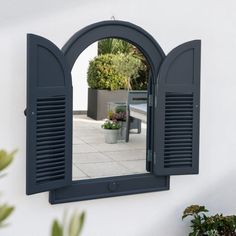 a mirror that is on the side of a wall with shutters and potted plants