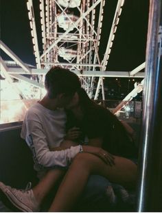 a man and woman sitting on top of each other in front of a ferris wheel