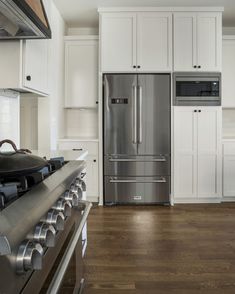 a stainless steel refrigerator and stove in a kitchen with white cabinets, wood flooring and hardwood floors