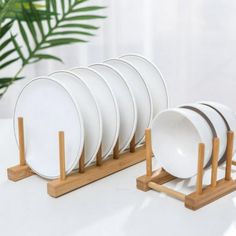 white plates are stacked on wooden stands next to a potted plant