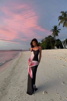 a woman standing on top of a sandy beach next to the ocean holding a pink ribbon