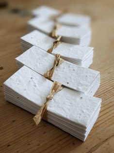 several pieces of white paper tied with twine on a wooden table, ready to be used as place cards