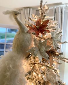 a white christmas tree decorated with silver and red leaves, feathers and lights in the shape of a peacock