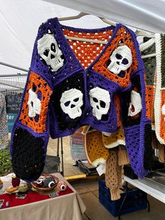 a crocheted sweater with skulls and bones hanging from it's sides at an outdoor market