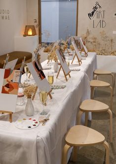 there are many easels on the table with paintings and wine glasses in front of them