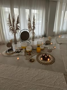 a room with candles and decorative objects on the floor in front of large window curtains