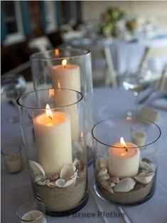 two clear vases filled with sand and lit candles on top of a white table cloth