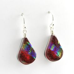 These handmade dichroic glass wide tear shaped earrings that we call lotus are a beautiful rainbow red color that shimmer in the light. Dangle earrings are 1 3/8 inches long and 1/2 inch wide. Earrings come with a pair of clear rubber earring stoppers for the ear wires. To clean: simply polish silver with a jewelry care cloth. Style Number: 17699 Metal: 925 Sterling Silver Dimensions: 1 3/8 inches long and 1/2 inch wide Handmade in North Carolina, USA Rainbow Lotus, Polish Silver, Beautiful Rainbow, Dichroic Glass, Sterling Earrings, Resin Jewelry, Ear Wires, Jewelry Care, Fashion Earrings