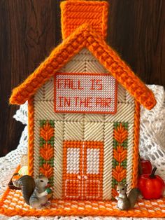 an orange and white house with two mice on the ground next to it, in front of a lace doily