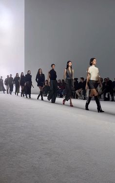 several models walk down the runway in black and white outfits, while others stand behind them