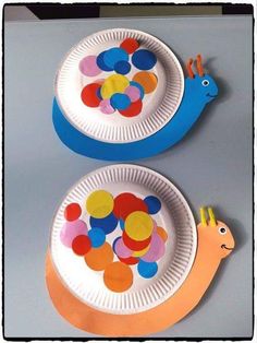 two paper plates decorated with colorful circles and a snail on them, one is white