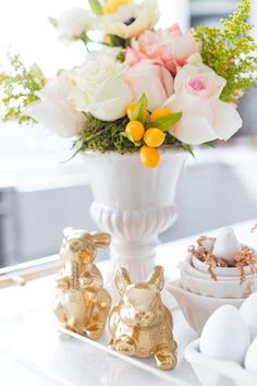 a white vase filled with flowers and gold bunny figurines on top of a table