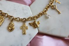 The Divinity Charm Bracelet is crafted from 18k gold-plated stainless steel and features a collection of vintage-inspired charms, including cherubs, crosses, and wings. Each charm is intricately designed to evoke a sense of timeless grace and beauty. Hypoallergenic and gentle on sensitive skin, this bracelet offers elegance and comfort for everyday wear. 18K Gold Plated Stainless Steel Materials Tarnish Resistant 8mm Chain Standard 7" Length With Love From Texas Gold James Avery Charm Bracelet, Vintage Gold Rosary Bracelet Gift, Vintage Gold Rosary Bracelet As A Gift, Vintage Gold Rosary Bracelet For Gift, Luxury Gold Charms With Vintage Charm, Luxury Vintage Charm Bracelet As Gift, Gold Spiritual Bracelet With Vintage Charm, Gold James Avery, Charm Bracelet Aesthetic