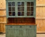 an old green china cabinet with glass doors and drawers in front of wood paneled walls