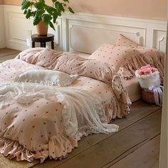 a bed with pink comforters and pillows on the floor next to a potted plant