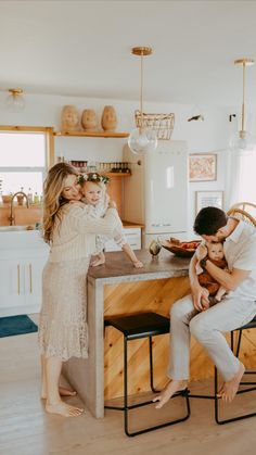 a man and woman sitting at a kitchen counter with a baby in their lap, while two other people stand nearby