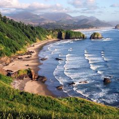 the beach is surrounded by lush green hills and water with waves coming in from the ocean