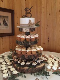 a wedding cake and cupcakes on a table in front of wood paneled walls