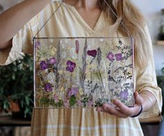 a woman holding up a painting with flowers on it in front of her face and hands