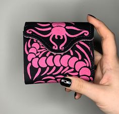 a woman's hand holding a pink and black wallet with an intricate design on it