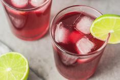 two glasses filled with red liquid and limes