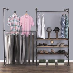 an open closet with clothes and shoes hanging on the rack, in front of a gray wall