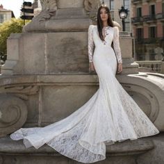 a woman in a white wedding dress standing next to a stone fountain with her hands on her hips