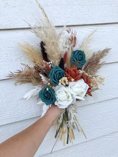 a hand holding a bouquet of flowers on top of a white wall