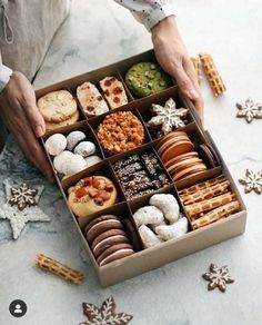 a person is holding an open box of cookies and pastries on a table with snowflakes