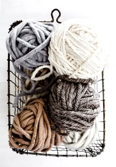 several balls of yarn in a wire basket on a white surface with a black hook