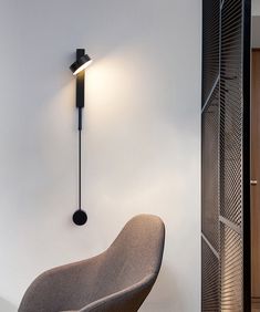 a modern wall light mounted on the side of a white wall next to a chair