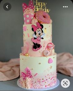 a three tiered cake decorated with minnie mouse and pink frosting