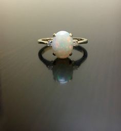 an opal and diamond ring sitting on top of a black surface with its reflection