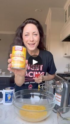 a woman holding up a can of food in front of a bowl and blender