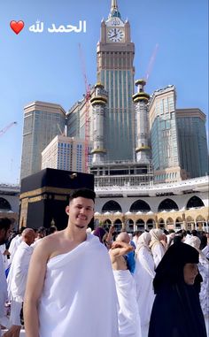 a man in a white robe standing in front of a building with a clock on it