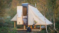 a tent is set up in the middle of some trees and bushes, with its door open