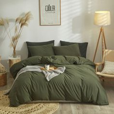 a bed with green sheets and pillows in a room next to a chair, rugs and lamp