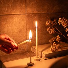 a person holding a lit candle in front of a book on a table with flowers