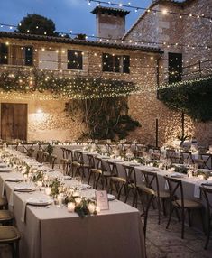 an outdoor dining area with long tables and lights strung from the ceiling above it, along with candles lit up on each table