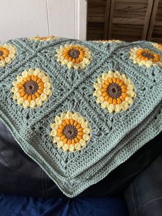 a crocheted blanket with sunflowers on it sitting on a black leather chair