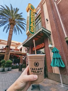 a hand holding up an ice cream sundae in front of a building with palm trees