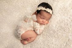 a baby is laying down on a white blanket wearing a lace headband and dress